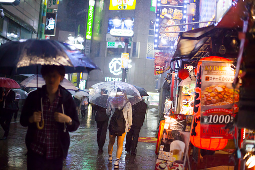 Tokyo, Japan- May 11, 2015: People with umbrellas walking under Noul typhoon rain on the street next to Shibuya crossing in Tokyo.