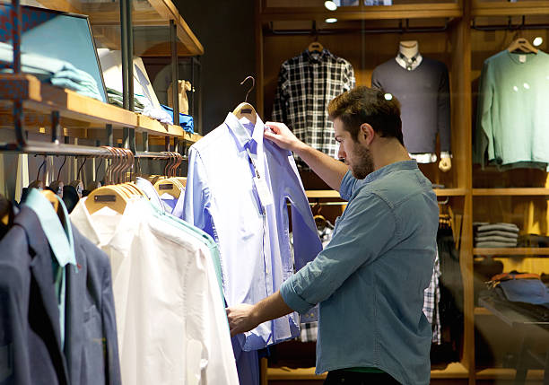 jeune homme shopping pour les vêtements dans un magasin - department store clothing showroom people photos et images de collection