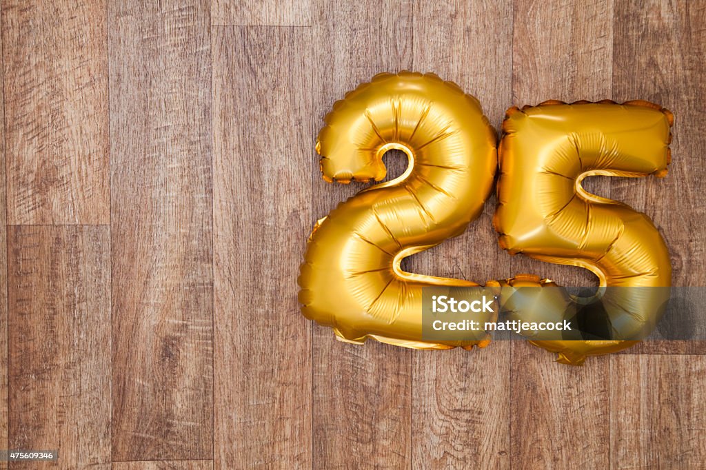 Gold number 25 balloon A gold foil number 25 balloon on a wooden background. The number is made from shiny golden foil and is inflated, it is on the right hand side of the image leaving copy space on the left of the image for your text or logo. 25-29 Years Stock Photo