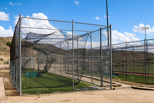 Batting cages with blue sky, puffy clouds and rolling hills Image of a fully enclosed batting cage.  Batting cages are used to practice hitting the ball in softball and baseball.  The sky overhead is blue with puffy cumulous clouds.  Inside the cage is green, fake turf.  The photo was taken in New Mexico. baseball cage stock pictures, royalty-free photos & images