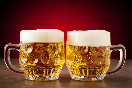 Two glasses of beer on a stone table over red background