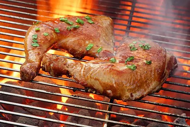 Close-up Overhead View On Two Tasty Roast And Smoked Chicken Quarters On The Hot Flaming BBQ Grill In The Background