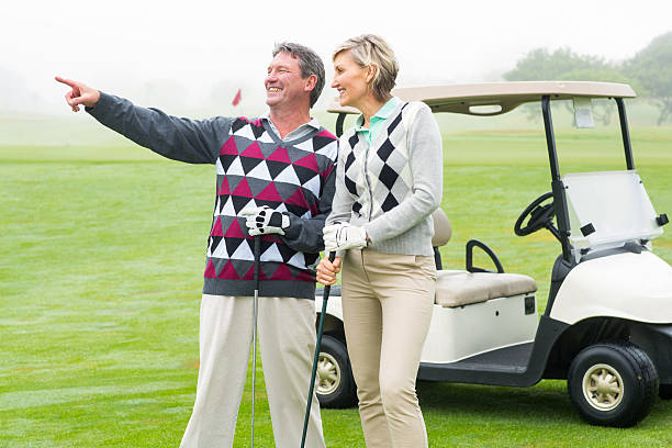 istock Happy golfing couple with golf buggy behind 475621304