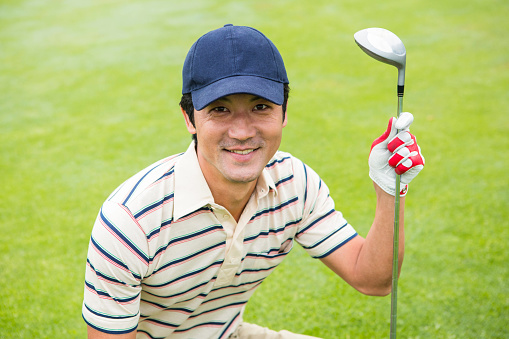 Crouching golfer smiling at camera and holding club at the golf course