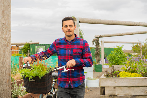 Young handsome man with plants and his bicycle arriving at his allotment. 