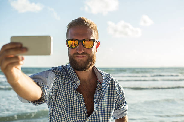 istock Beard man on beach at sunset taking selfie using telephone 475642972