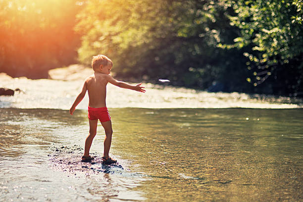 pulando de pedras-menino jogando no rio - throwing stone little boys child - fotografias e filmes do acervo