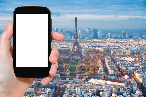 travel concept - tourist photographs view of Paris with Eiffel Tower on smartphone with cut out screen with blank place for advertising logo