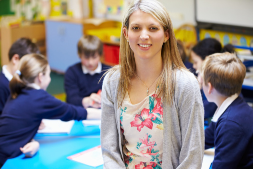 Portrait Of Teacher Smiling At Camera In Classroom With Pupils