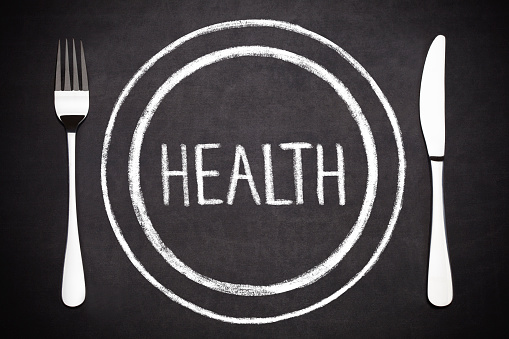 Health lettering on a plate with a fork and a knife on the side  drawing with chalk on blackboard.