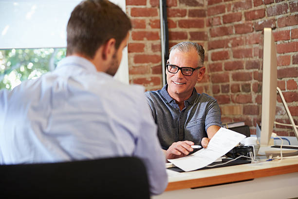 Businessman Interviewing Male Job Applicant In Office Happy Smiling Businessman Interviewing Male Job Applicant In Office casual job interview stock pictures, royalty-free photos & images
