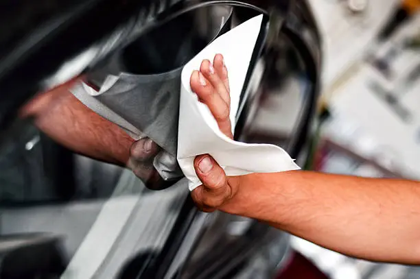 auto car worker and mechanic cleaning a cars window with special tool for scratches and wiper