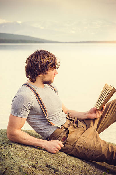 istock Young Man reading book outdoor 475669554