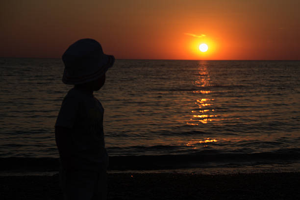 istock Little boy standing back and watching the sunset 475681886
