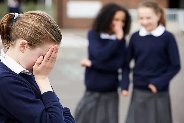 Female Elementary School Pupils Whispering In Playground About Another Girl