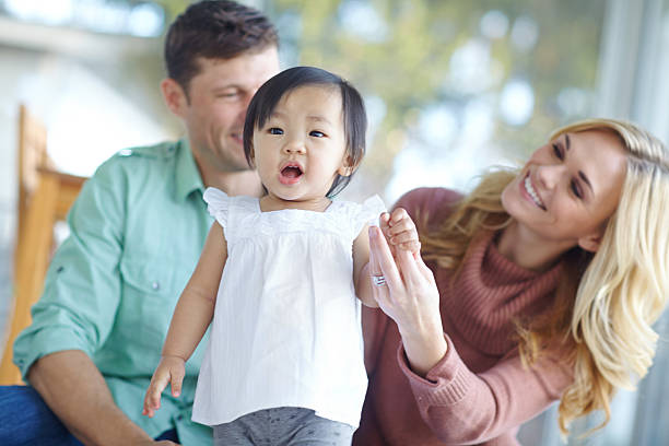 You can do it! A happy couple teaching their beautiful adopted daughter to walk while at home asian adoption stock pictures, royalty-free photos & images
