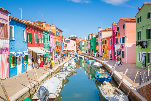 Burano Island, Venice, Italy - July 4, 2022: Tourists among the sovereign shops on the main street of burano Island,  Colorful houses on the canal. Famous travel destination.