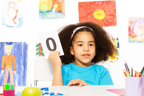 Photo of African girl holds flashcard with zero at  desk
