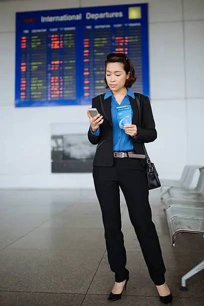 Full-length portrait of business lady with boarding pass reading a message