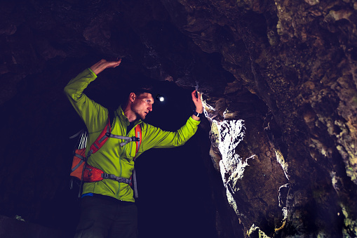 Man walking and exploring dark cave with light headlamp underground. Mysterious deep dark, explorer discovering mystery moody tunnel looking on rock wall inside.