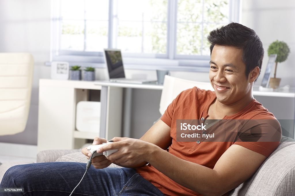 Playing video game Young Asian man sitting in armchair at home, playing video game, smiing.. 20-29 Years Stock Photo
