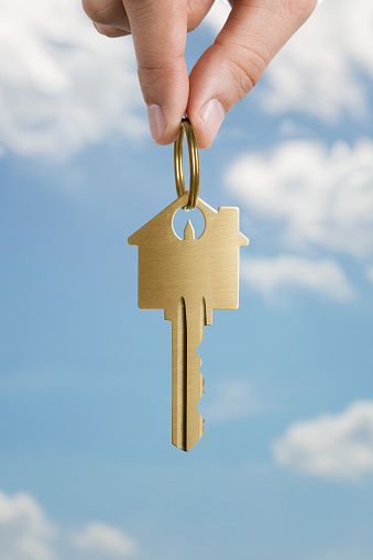 Close up of human hand holding key to a dream house over sky background