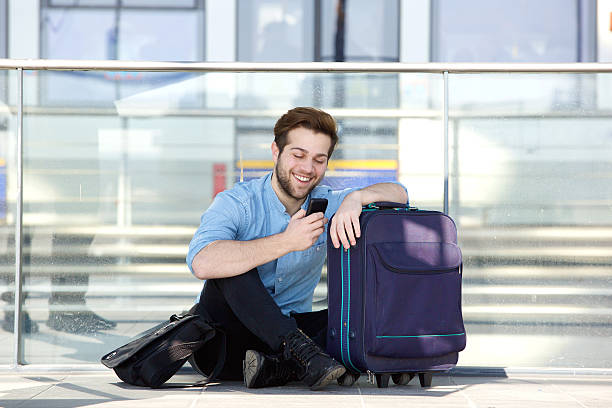 istock Happy man sitting on floor at station reading text message 475706976