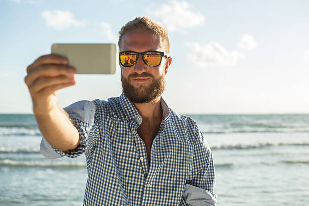 istock Young man on the beach at sunset taking a selfie 475719596
