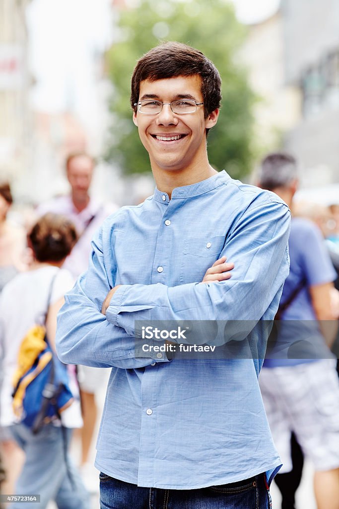 Young man with crossed arms outdoor Portrait of smiling guy in glasses with crossed arms at crowded street in a sunny day 2015 Stock Photo