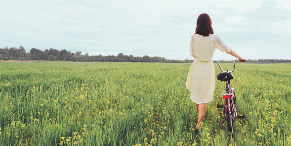 Girl in dress walking with bicycle on summer green meadow