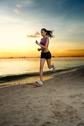 Woman at the beach running by the ocean at sunset