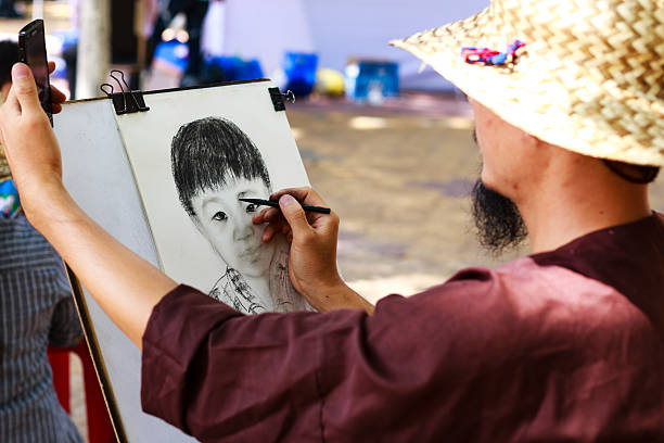 Ho Chi Minh city, Vietnam - May 28, 2015: Street artist drawing with a pencil, looked at the sample using smartphone at a park in the city