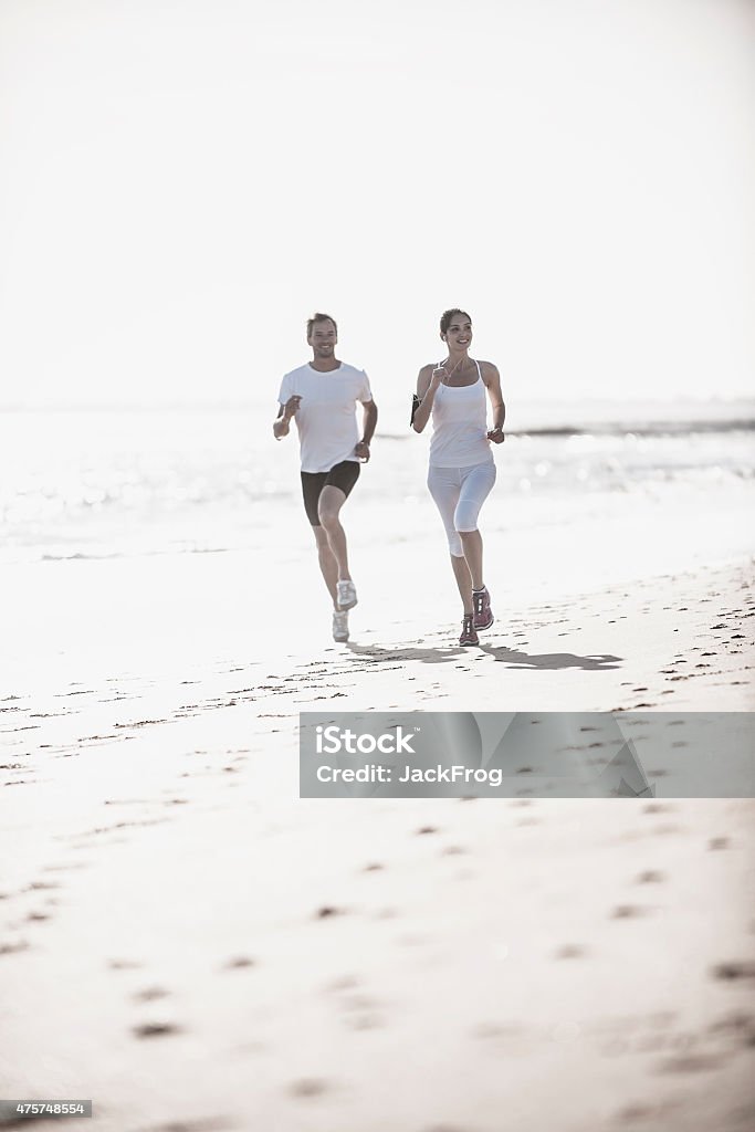 couple is jogging on the beach, woman listening to music a dynamic couple is jogging on the beach, woman listening to music on her smartphone 2015 Stock Photo