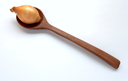 Onion on wooden spoon with space on white background