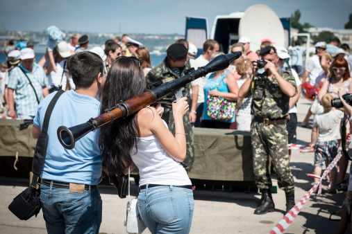 Sevastopol, Crimea, Ukraine - July 28, 2013: During the annual Navy Day event at the Black Sea port of Sevastopol, a civilian woman poses with a rocket propelled grenade as a sailor takes her picture. Sevastopol, located in Ukraine, is home to both Russian and Ukrainian navies