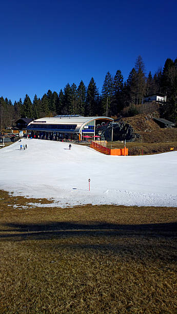 Skiing Garmisch, Partenkirchen - February 24, 2014: View of the Kreuzeckbahn, a cable railway station going up into a wide ski arena. The visible snow was created via snow canons. Some skier to be seen and a restaurant in front of the station. fake snow stock pictures, royalty-free photos & images