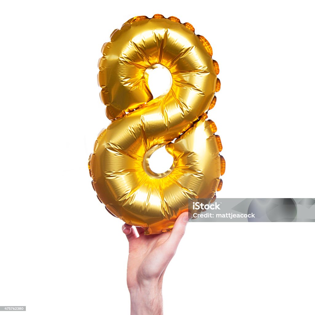 Gold number 8 balloon A gold foil number 8 balloon is held by a caucasian male hand. The number is being held at the base. The number is made from shiny golden foil and is inflated. The background is plain white. 2015 Stock Photo