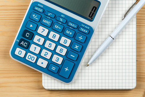 Close-up of blue and white calculator, notepad with pencil on wooden background.