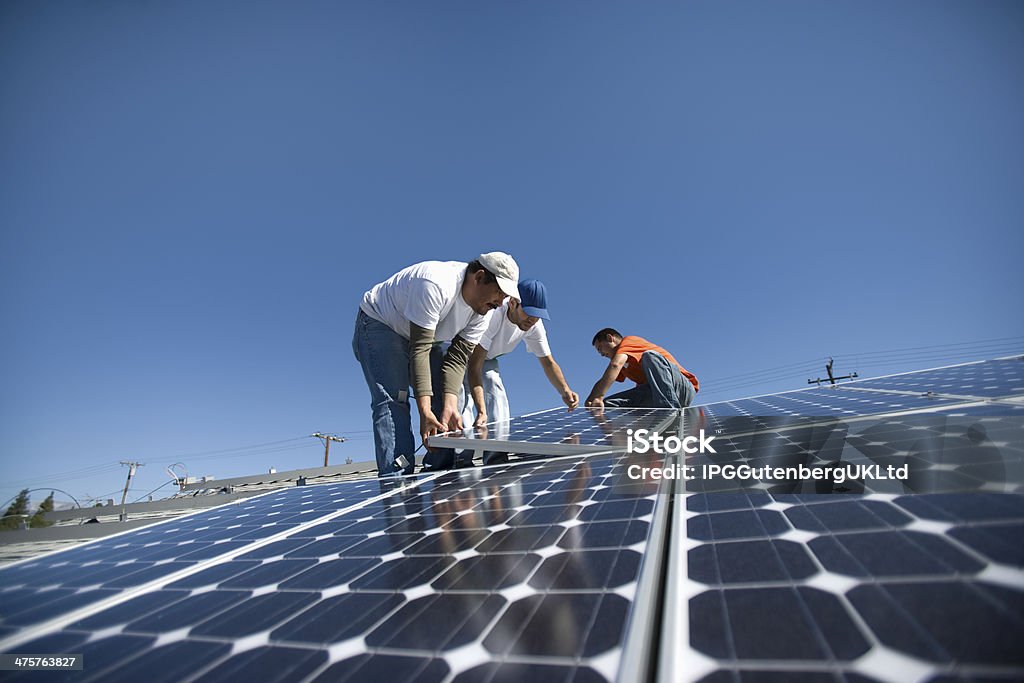 Engineers Placing Solar Panel Against Sky Interracial engineers placing solar panel against clear blue sky USA Stock Photo