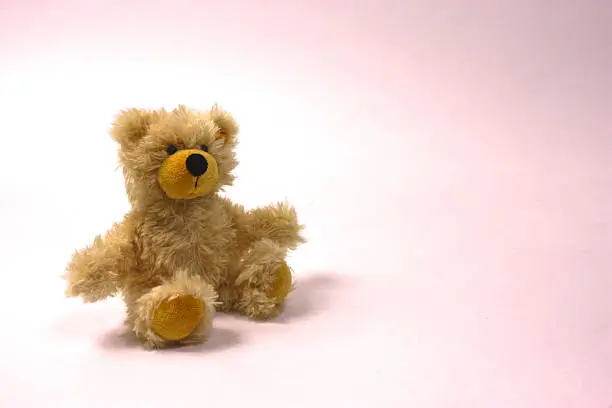 Teddy bear, beige/gold colored, sitting alone, white and pinkish background