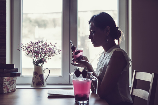 Silhouette of a woman that is drinking lemonade at home. Candid shot. Low key portrait.