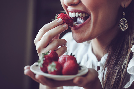 Young Latin woman tasting delicious strawberries. Close-up, candid shot. 