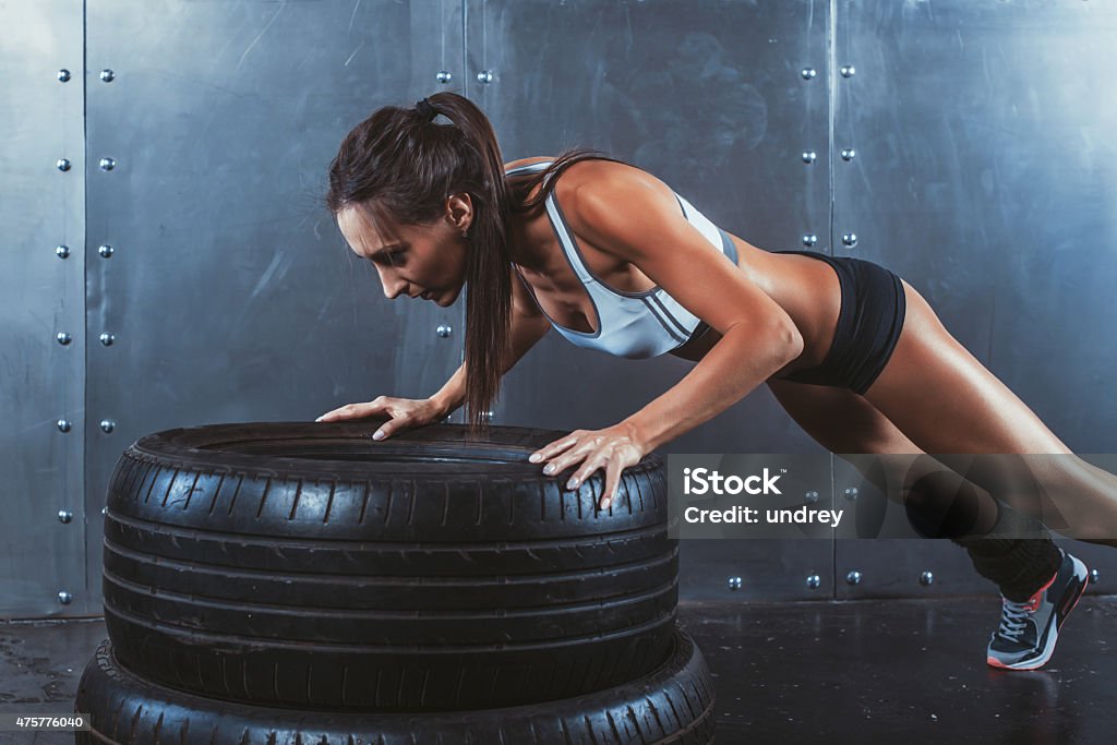 Sportswoman. Fit sporty woman doing push ups on tire strength Sportswoman. Fit sporty woman doing push ups on tire strength power training concept gym fitness workout sport and lifestyle  2015 Stock Photo