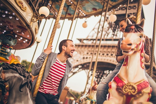 Young loving couple on carousel in Paris, France with an Eiffel tower in the background.