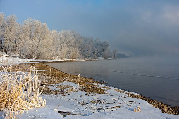 istock The snow-covered grass and trees on the river bank 475781179