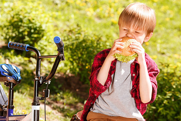 istock Boy biting off sandwich in park 475788326