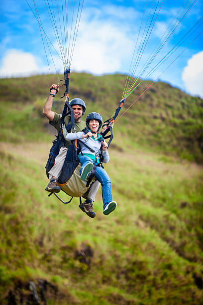 junges paar, die imposante-tandem-gleitschirmfliegen - gleitschirmfliegen stock-fotos und bilder