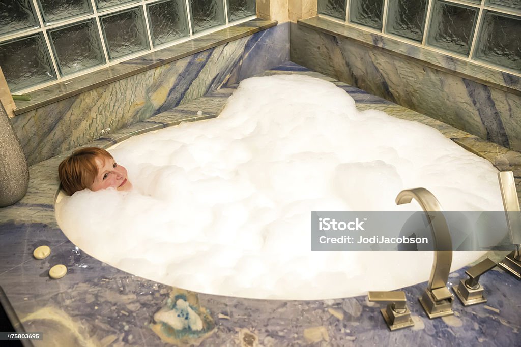 Woman taking a bubble bath A woman having a relaxing bubble bath in a large, round tub.  RM Adult Stock Photo