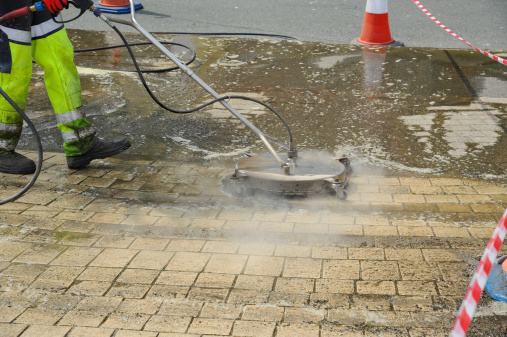 Torquay, United Kingdom - April 26, 2011: A Street cleaner wearing protective clothing using a high pressure steam jet wash cleaner to blast clean the sidewalk removing all of the surface dirt and stains.