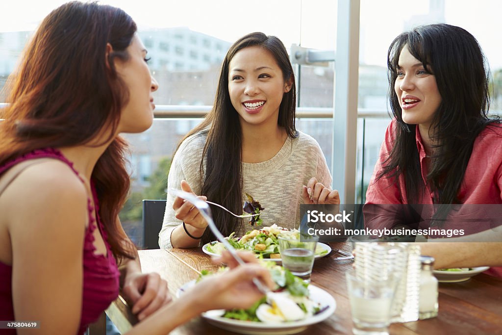 Three Female Friends Enjoying Lunch At Rooftop Restaurant Three Female Friends Enjoying Lunch At Rooftop Restaurant Chatting With Each Other. Restaurant Stock Photo